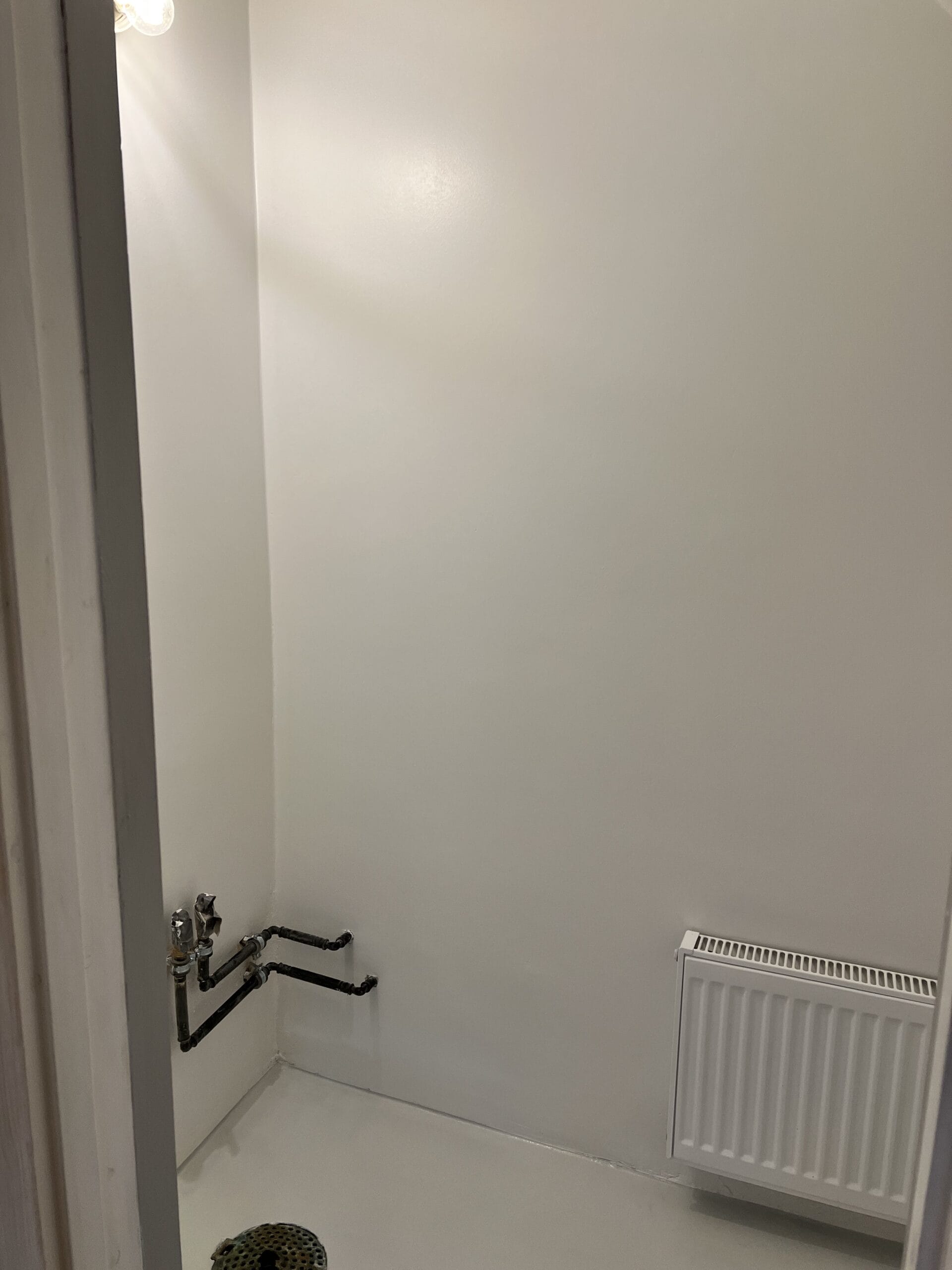 Lille hvidt rum med radiator og rørinstallation