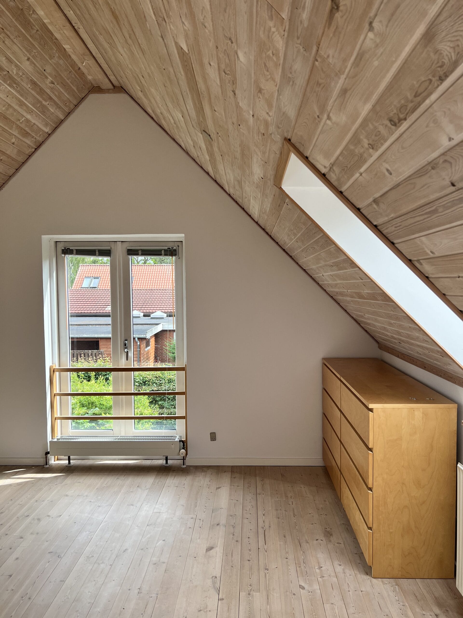 Lyst loftsrum med træloft og kommode